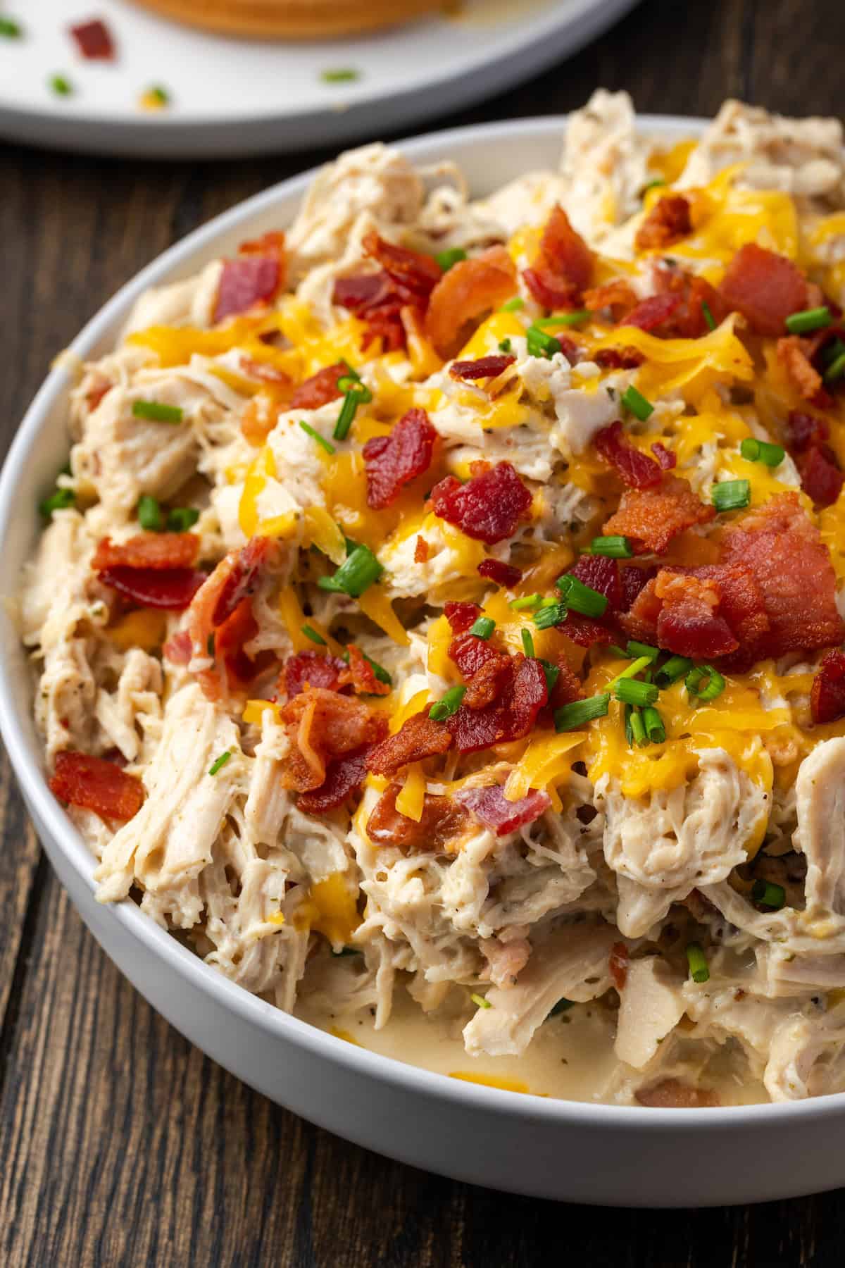 A bowl of Instant Pot crack chicken topped with crumbled bacon, cheese, and chives.