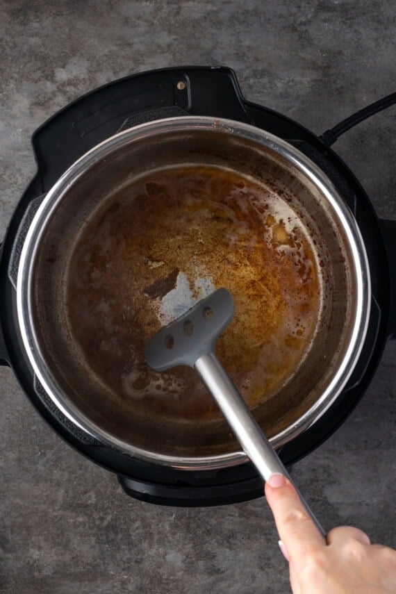 A spatula is used to scrape the browned bits from the bottom of the instant pot after deglazing with broth.