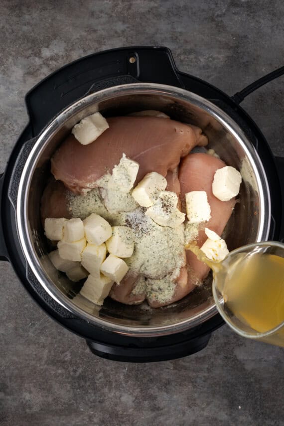 Chicken broth is poured over crack chicken ingredients in the instant pot.