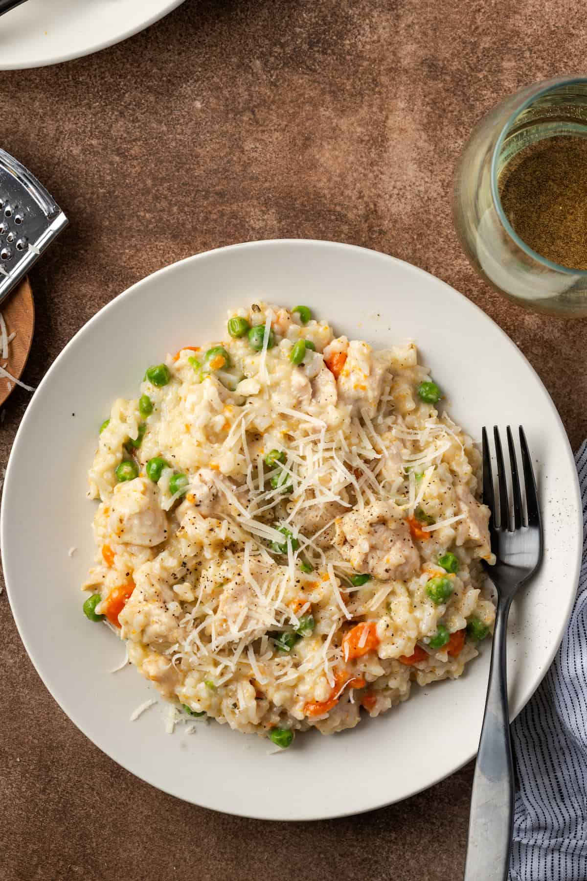 Overhead view of instant pot chicken and rice in a white bowl next to a stemless glass of white wine.