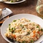 Instant pot chicken and rice in a white bowl next to a stemless glass of white wine, with a second bowl in the background.