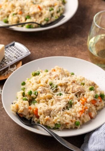 Instant pot chicken and rice in a white bowl next to a stemless glass of white wine, with a second bowl in the background.