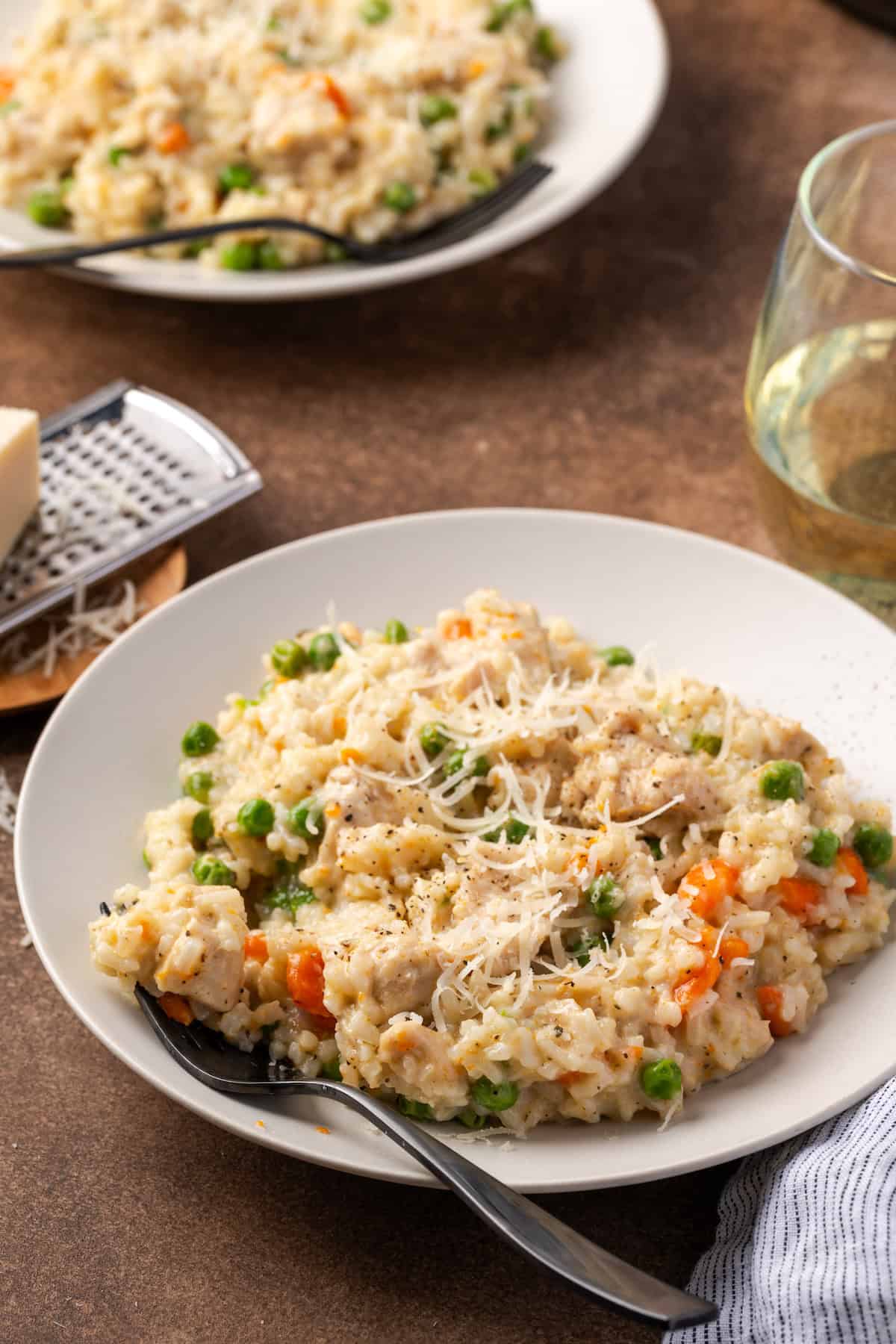 Instant pot chicken and rice in a white bowl next to a stemless glass of white wine, with a second bowl in the background.