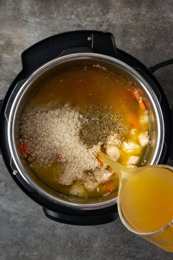 Chicken stock is poured over chicken and rice ingredients inside the instant pot.