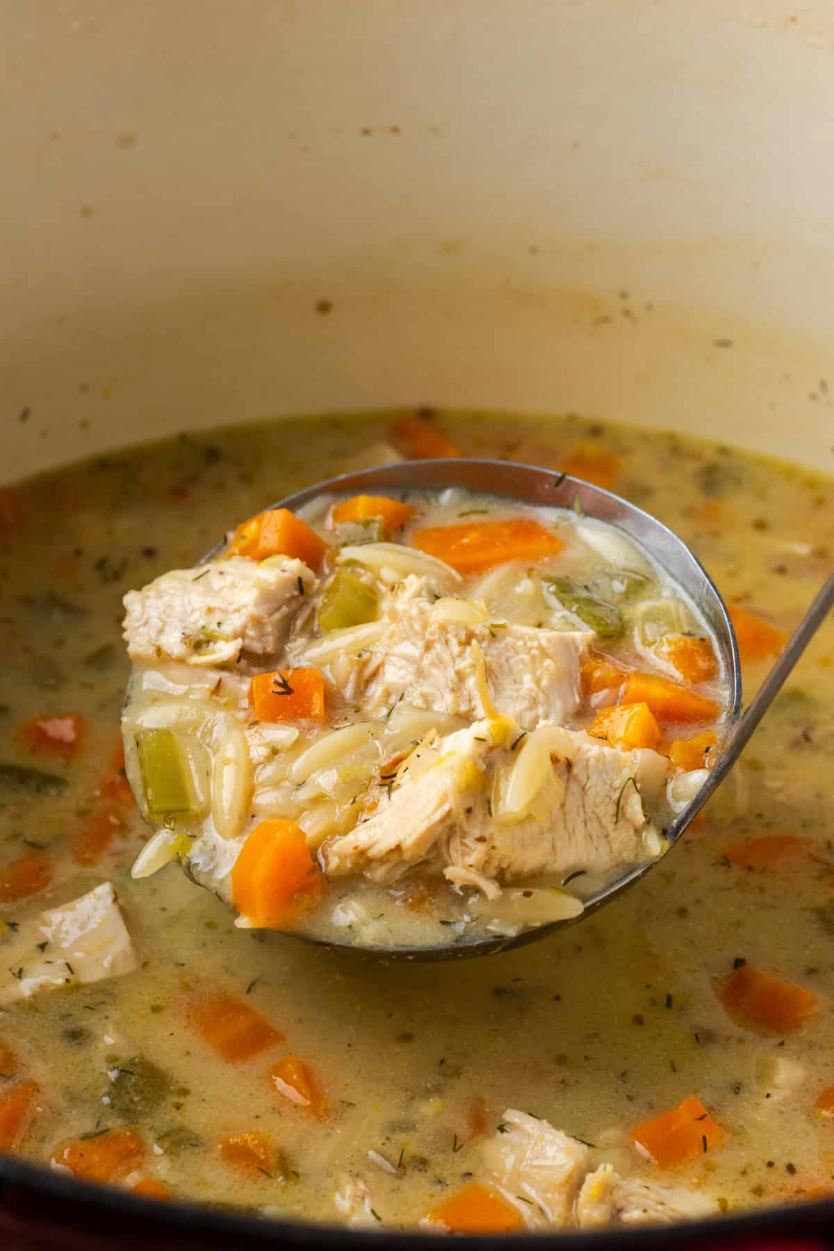 A ladle lifting lemon chicken orzo soup from a large pot of soup.