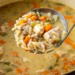 A ladle lifting lemon chicken orzo soup from a large pot of soup.