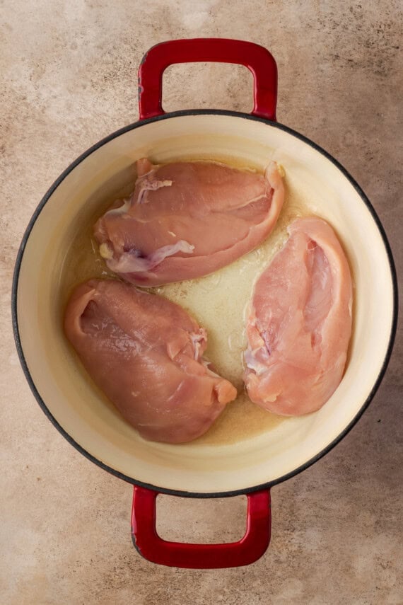 Three chicken breasts searing in a large pot.
