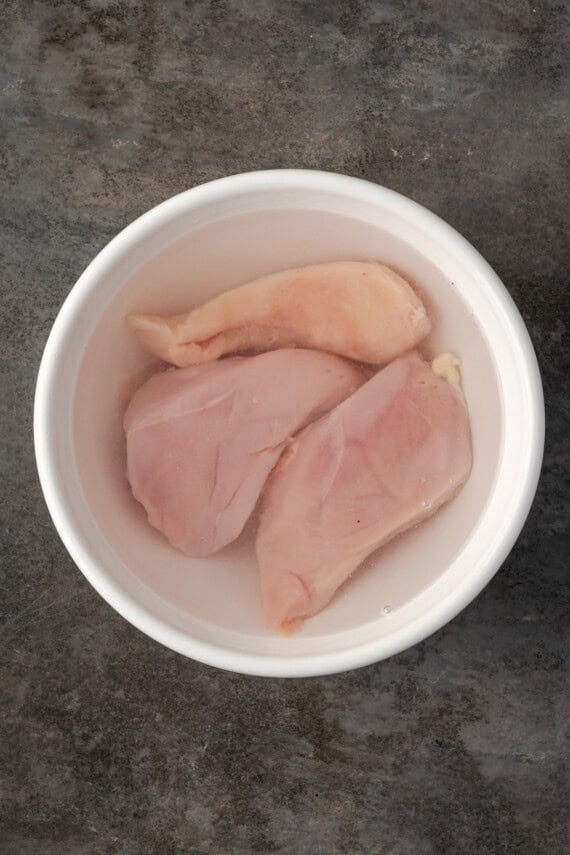 Chicken breasts soaking in a large bowl of salted brine.