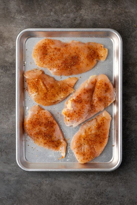 Brined and seasoned chicken breasts arranged on a metal baking sheet.