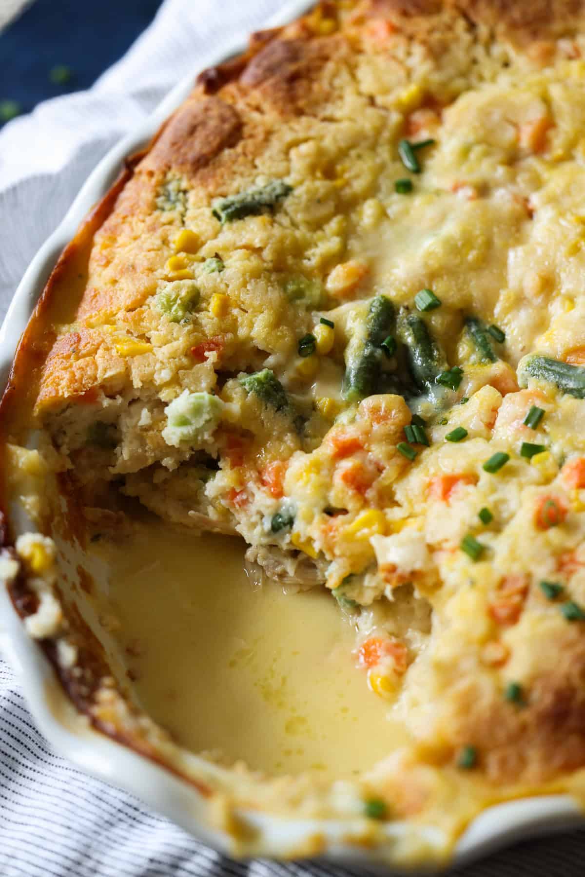 A baking dish with chicken cobbler and a piece missing showing the gravy the recipe makes while baking