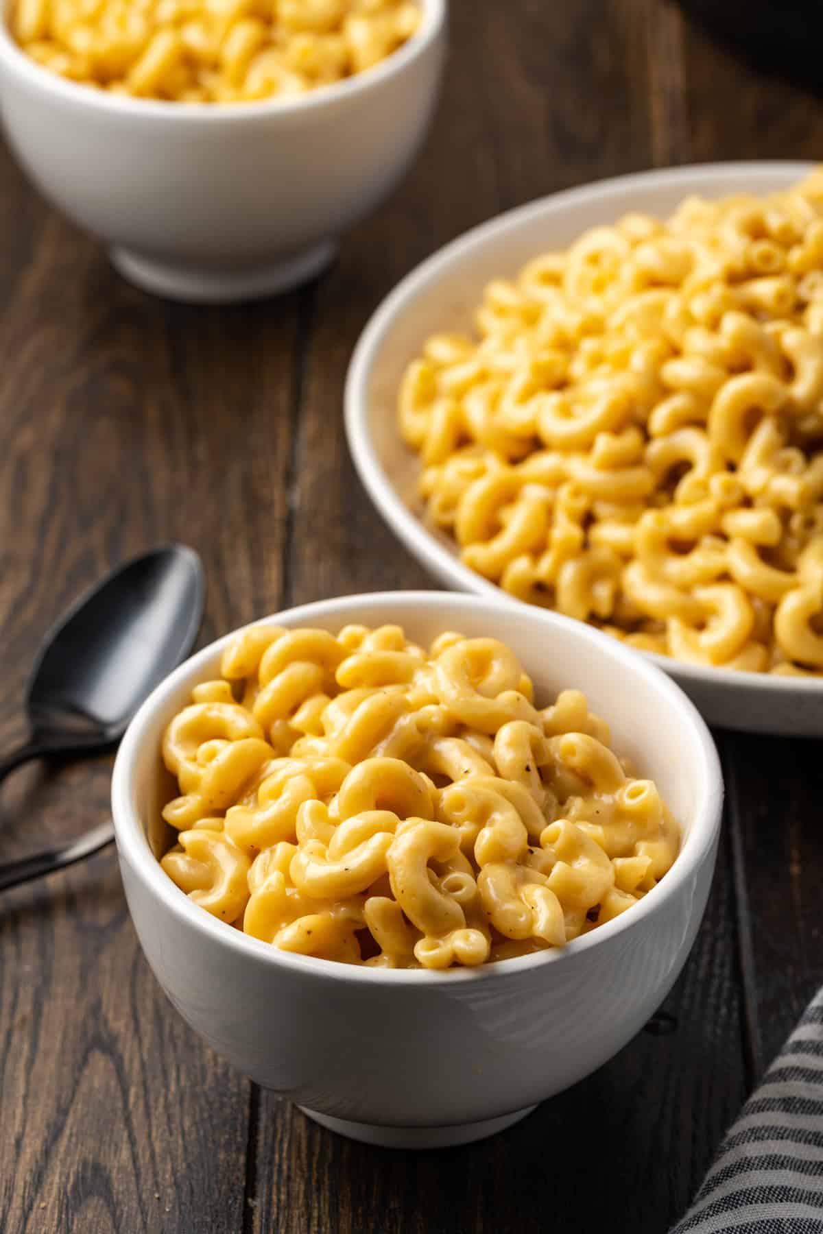 Three bowls of Instant Pot mac and cheese next to spoons on a wooden countertop.