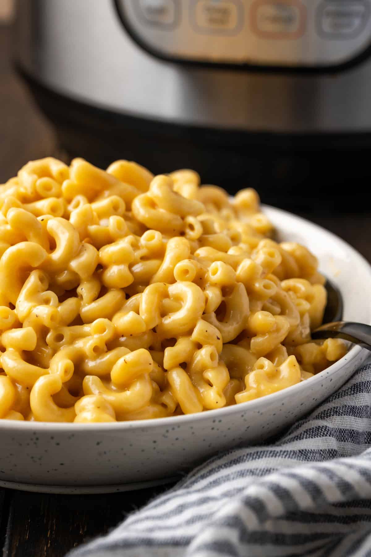 Instant Pot mac and cheese in a large bowl with a spoon, with the Instant Pot in the background.