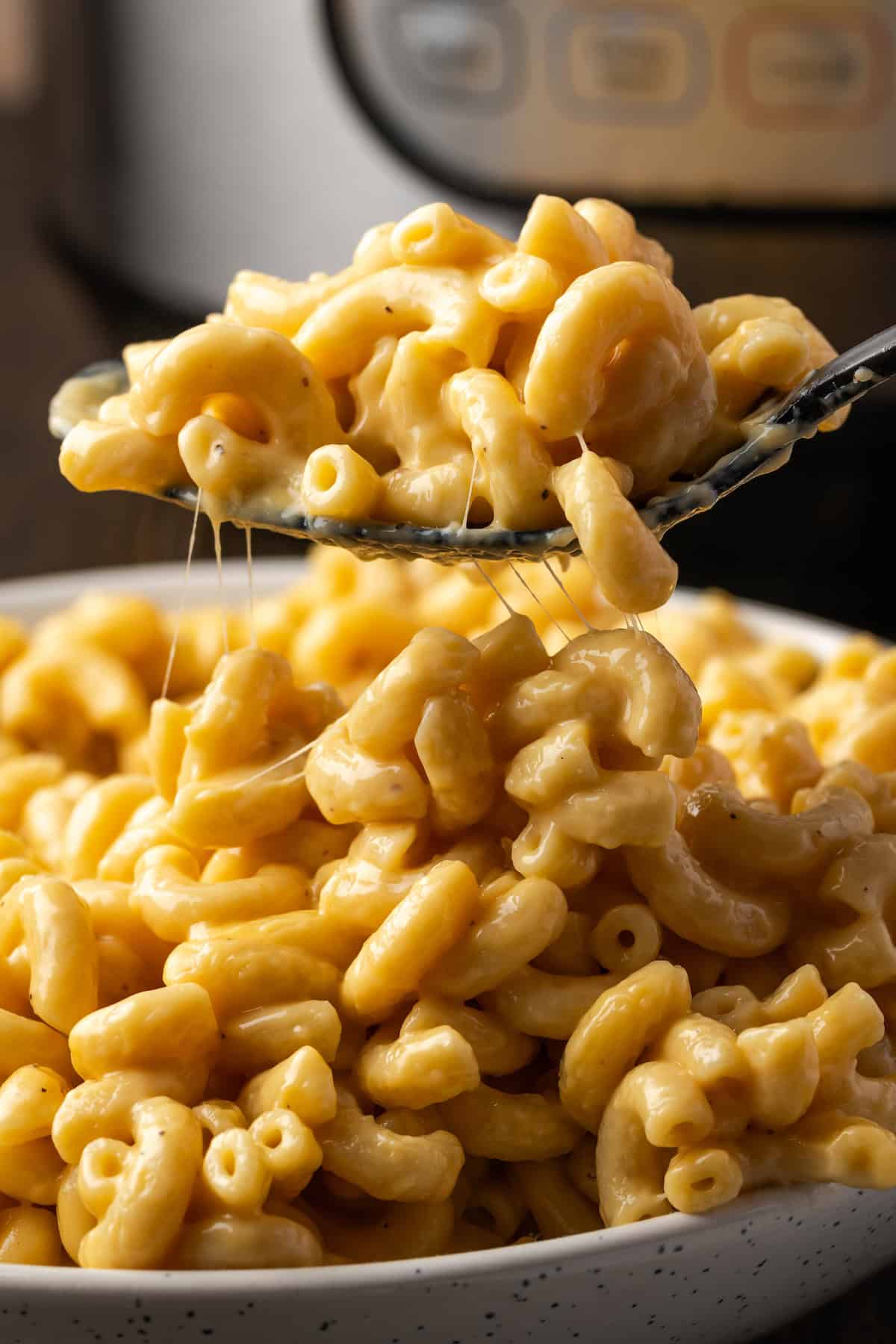 A spoonful of mac and cheese held above more mac and cheese in a bowl, with the Instant Pot in the background.