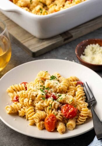 A bowl of Boursin cheese pasta, next to a small dish of parmesan and a glass of wine, with a casserole dish in the background.