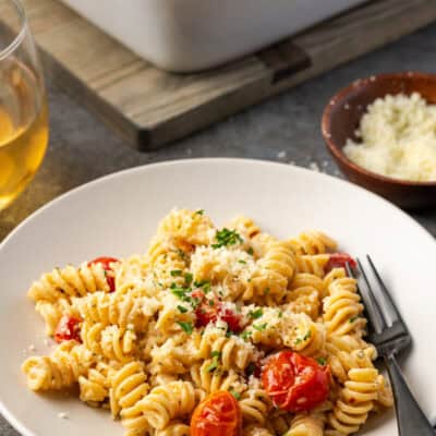 A bowl of Boursin cheese pasta, next to a small dish of parmesan and a glass of wine, with a casserole dish in the background.