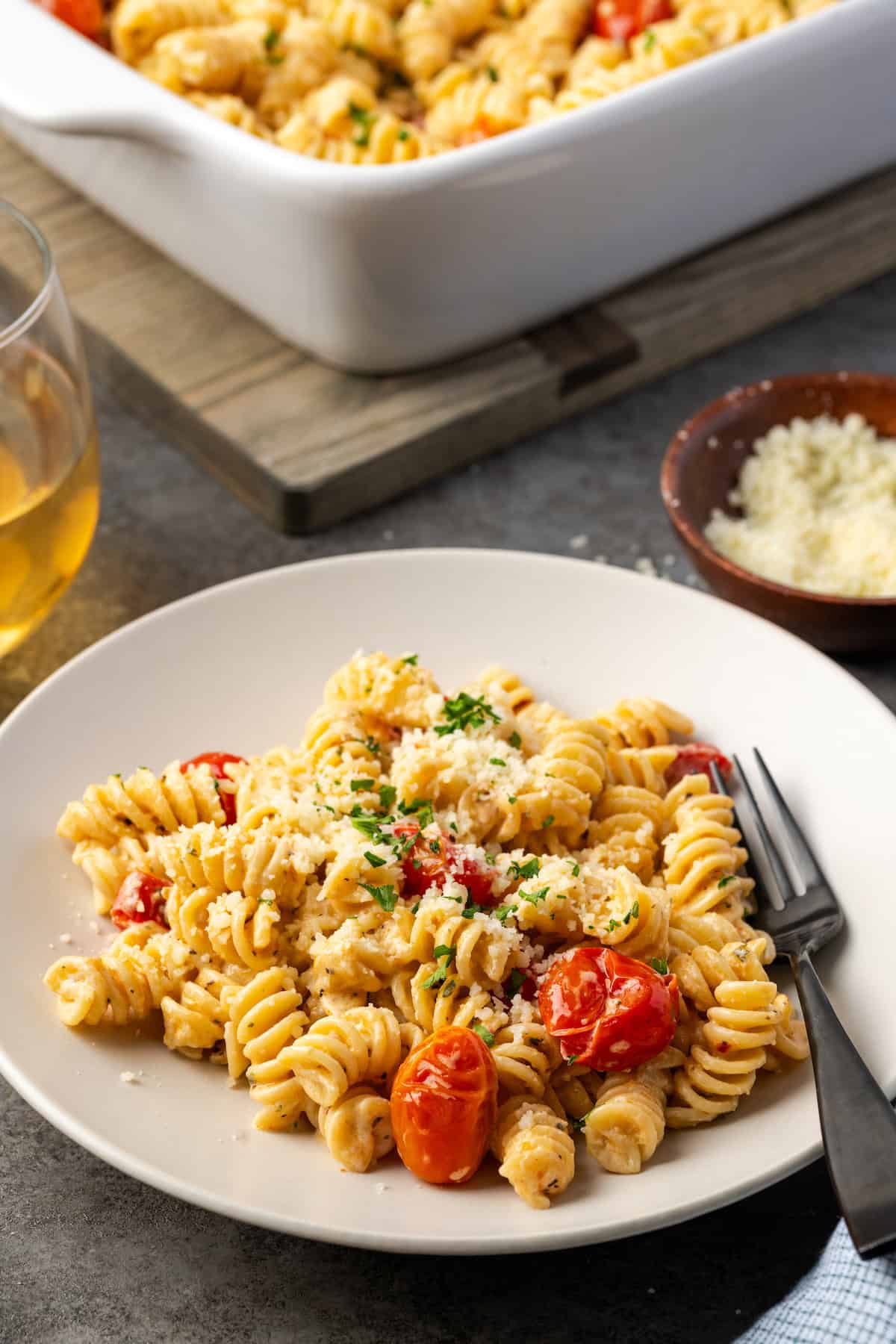 A plate of pasta with Boursin cheese, along with a small plate of parmesan and a glass of wine, with a casserole in the background.