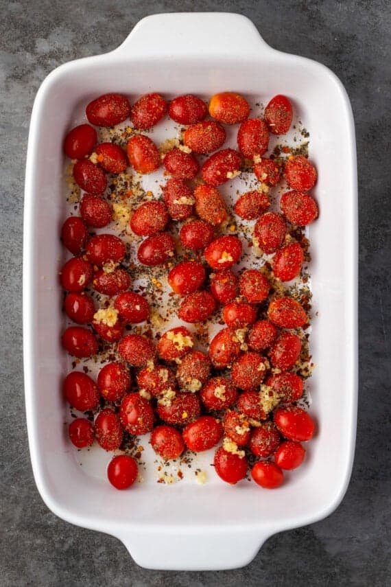 Cherry tomatoes and seasonings added to a baking dish.