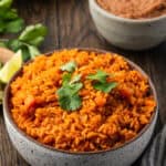 A bowl of Instant Pot Mexican rice with a plate of lime wedges, a bowl of refried beans, and flour tortillas in the background.
