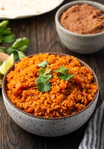 A bowl of Instant Pot Mexican rice with a plate of lime wedges, a bowl of refried beans, and flour tortillas in the background.