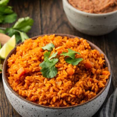 A bowl of Instant Pot Mexican rice with a plate of lime wedges, a bowl of refried beans, and flour tortillas in the background.