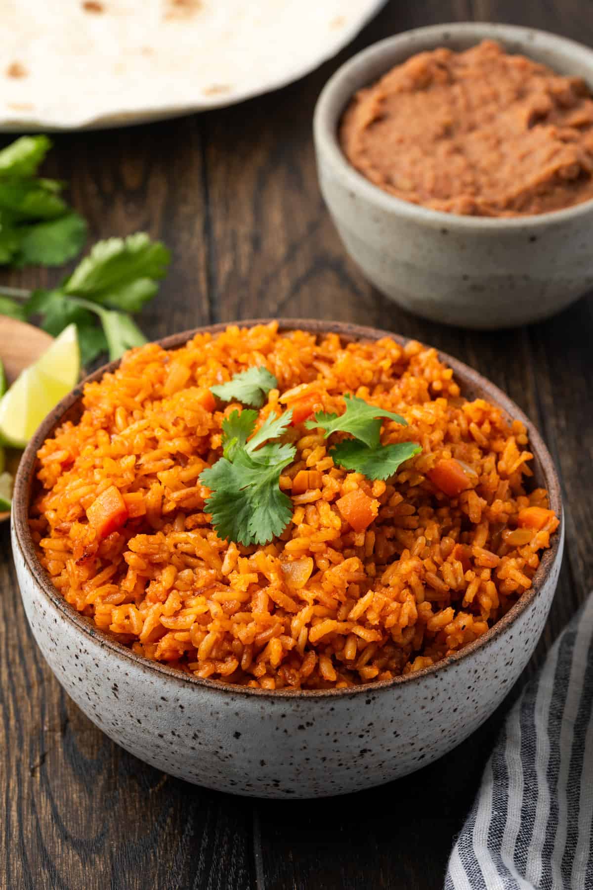 A bowl of Instant Pot Mexican rice with a plate of lime wedges, a bowl of refried beans, and flour tortillas in the background.