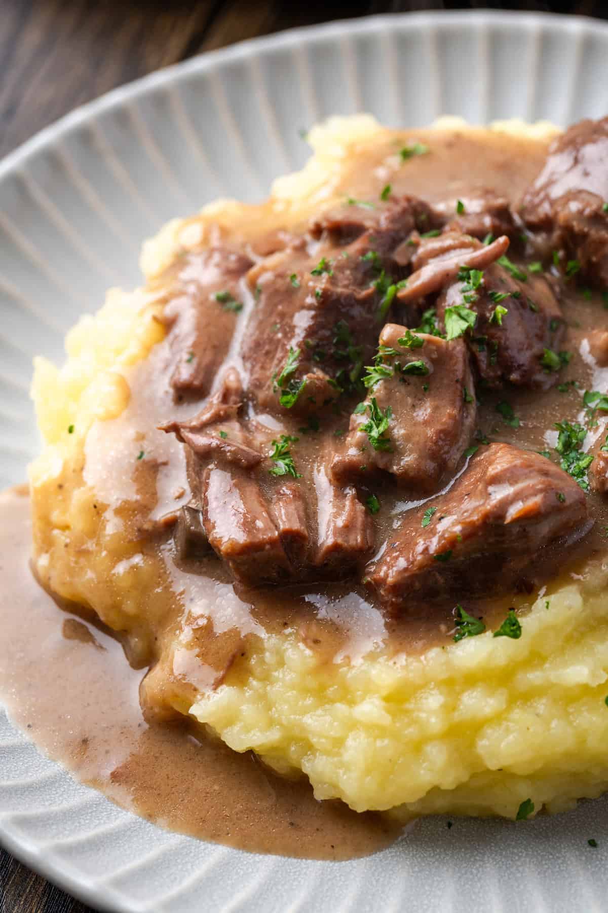 Close up of no peek beef tips and gravy served over mashed potatoes on a white plate.