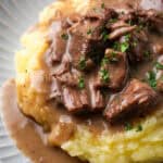 Close up of no peek beef tips and gravy served over mashed potatoes on a white plate.