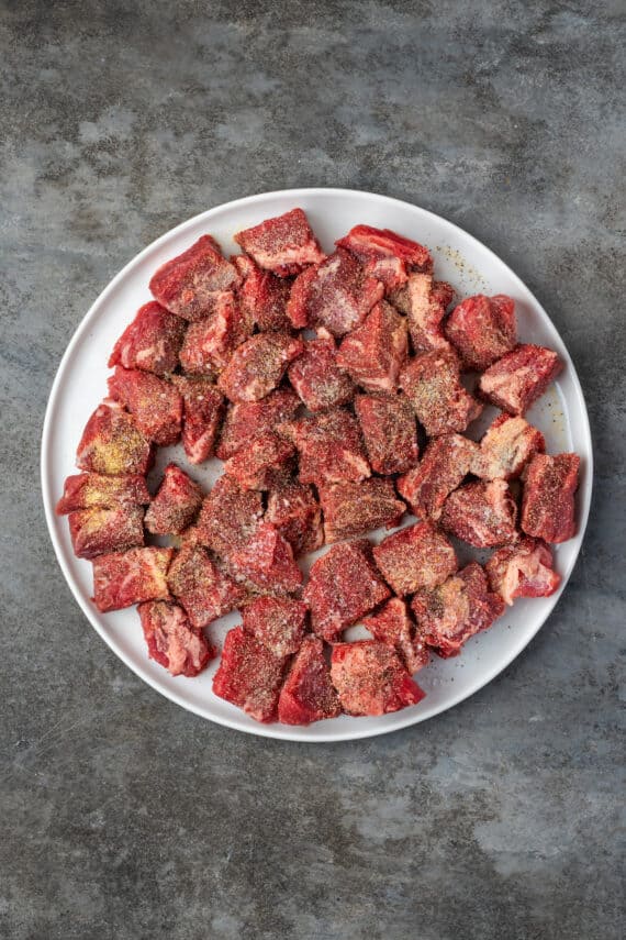 Season cubed beef on a large round plate.