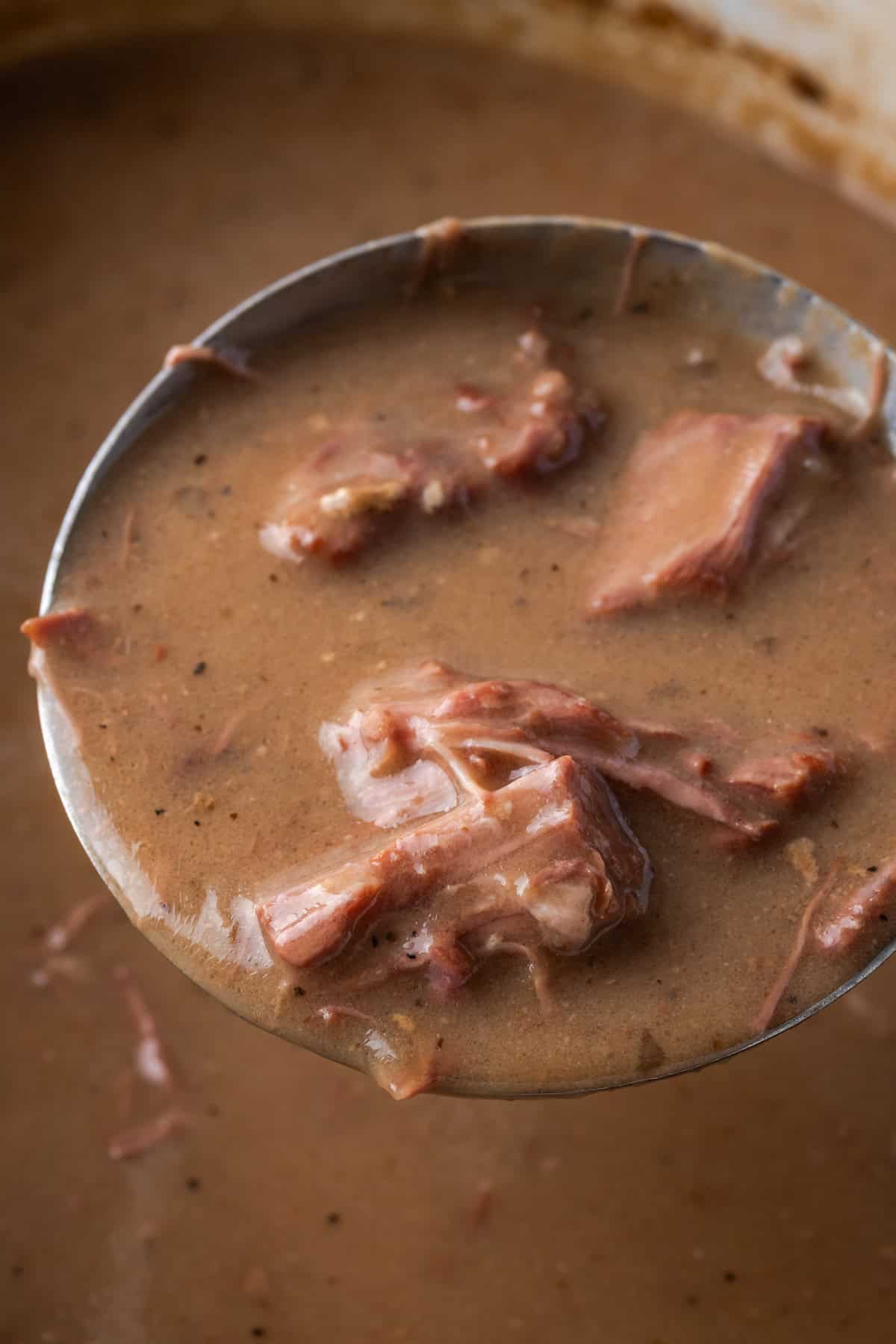 Close up of a ladle lifting a large scoop of no peek beef tips from a crock pot.