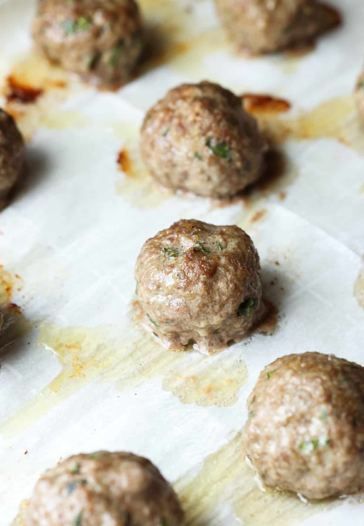 Baked meatballs on a parchment lined baking sheet