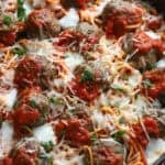 Spaghetti and Meatballs baked in a skillet topped with cheese and fresh parsley