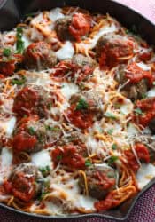 Spaghetti and Meatballs baked in a skillet topped with cheese and fresh parsley