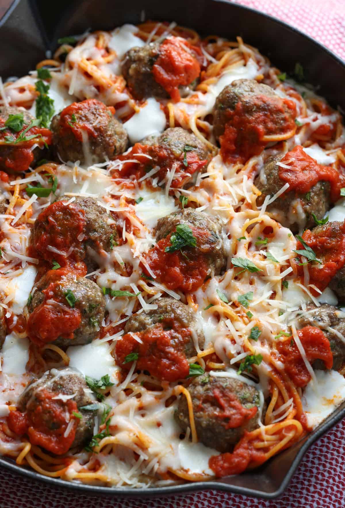 Spaghetti and Meatballs baked in a skillet topped with cheese and fresh parsley