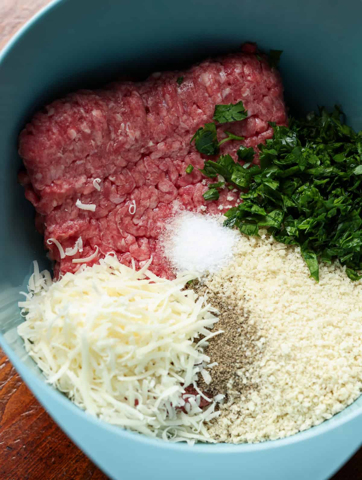 Meatball ingredients (ground beef, parmesan cheese, panko breadcrumbs, seasonings, and parsley) in a blue bowl