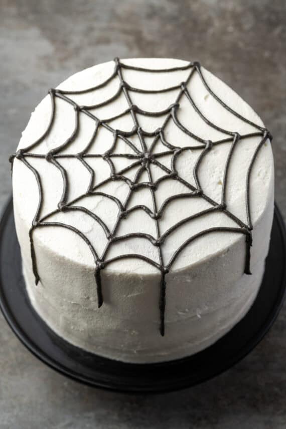 A spider web piped with black frosting over a white layer cake.