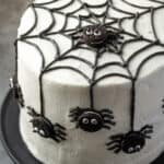 A spider cake topped with a black frosting web and mini Oreos decorated to look like spiders.