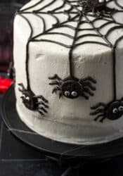 A spider cake topped with a black frosting web and mini Oreos decorated to look like spiders.