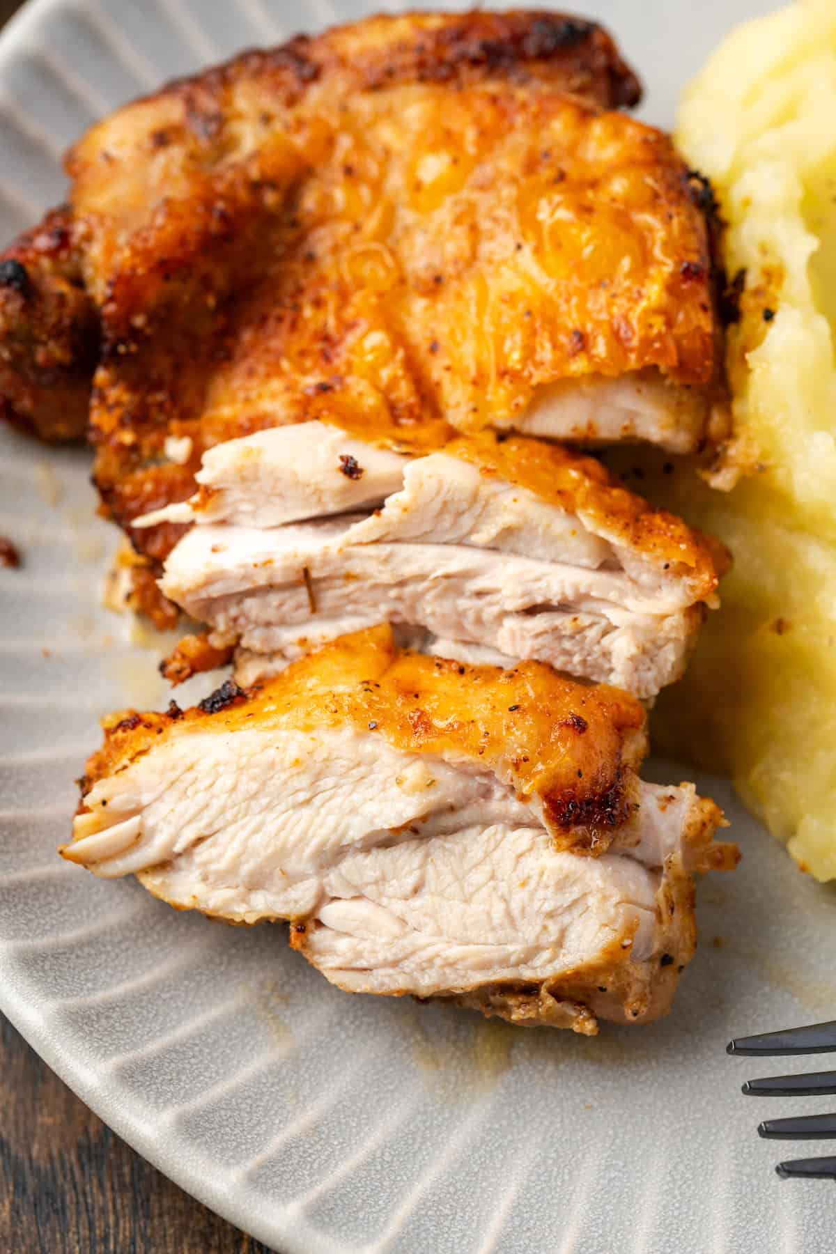 Close up a sliced ​​chicken thigh next to mashed potatoes on a plate.