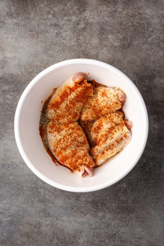 Seasonings added to chicken thighs in a bowl.