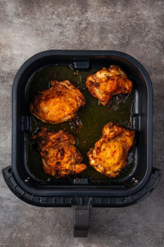 Four cooked chicken thighs inside the air fryer.