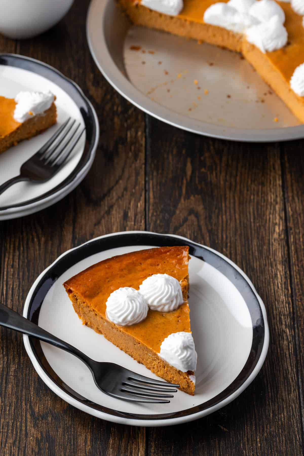 A slice of forkless pumpkin pie with a fork on a plate, the rest of the pie in the background.