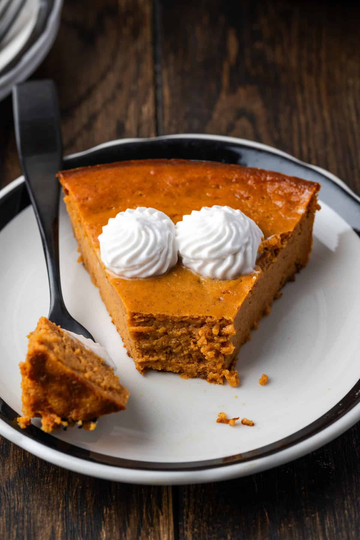 A crusty pumpkin pie next to a slice of crustless pumpkin topped with whipped cream pie on a plate.