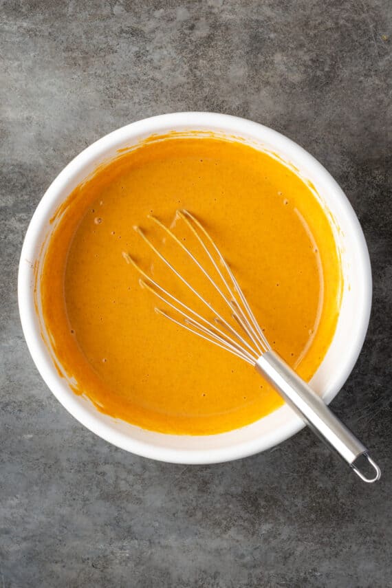 Pumpkin pie filling in a white bowl with a whisk.