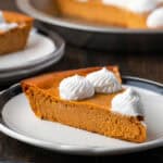 A slice of crustless pumpkin pie on a plate with a fork, with the rest of the pie in the bakground.