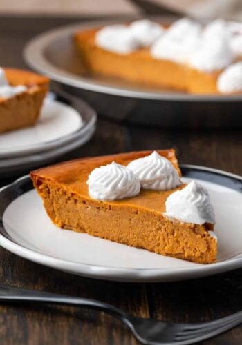 A slice of crustless pumpkin pie on a plate with a fork, with the rest of the pie in the bakground.