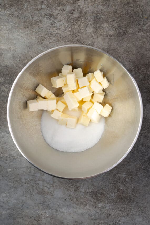 Cubed butter added to sugar in a metal bowl.