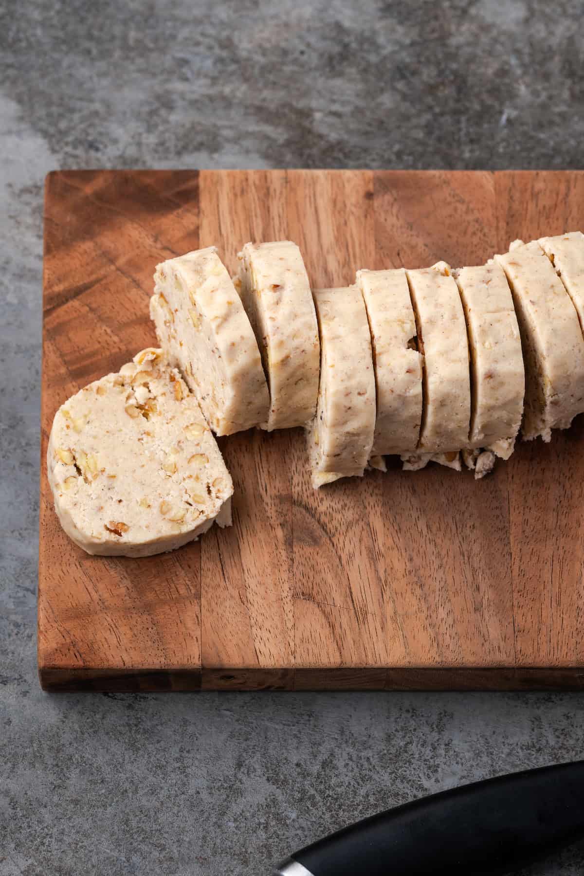 Pecan sandies are buttery, crumbly shortbread cookies with crispy edges and plenty of nutty crunch. They make great Christmas cookies! A log of pecan sandies cookie dough sliced into cookies on a wooden cutting board.