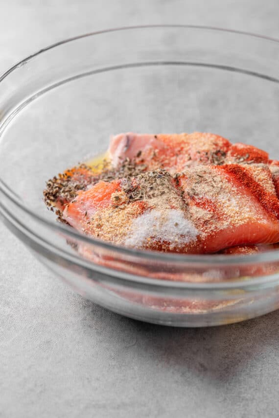 Salmon fillets and spices in a glass bowl.