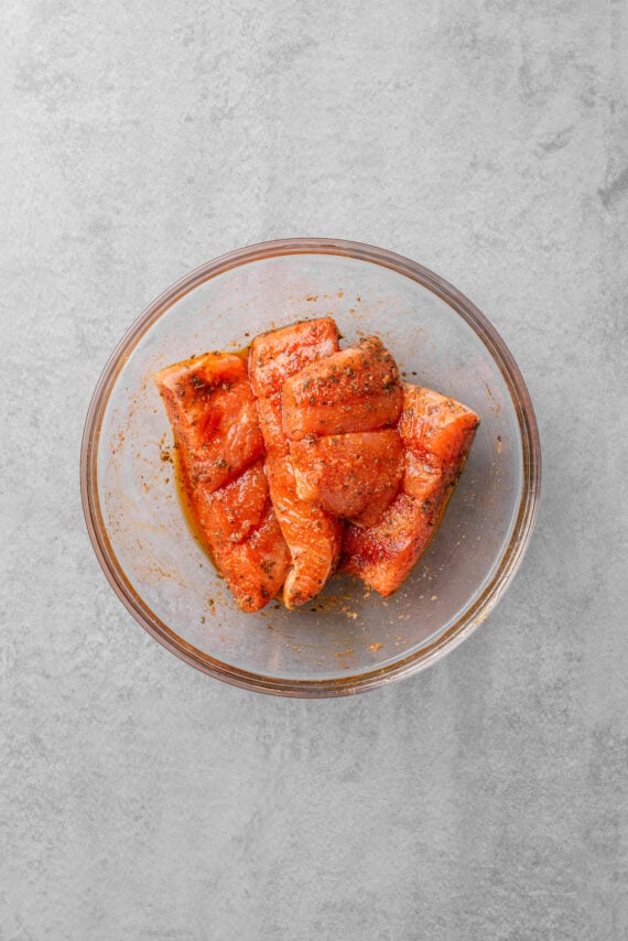 Raw salmon covered with seasonings in a glass bowl.