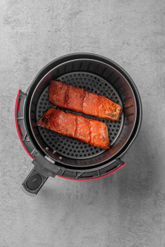 Two raw salmon fillets ready to be cooked in an air fryer basket.